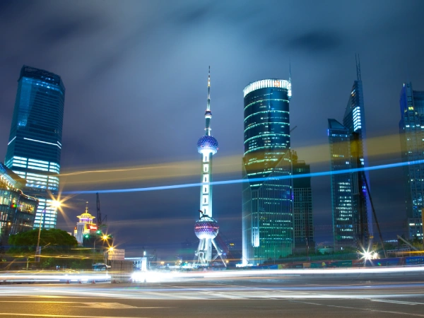 light-trails-street-by-illuminated-buildings-against-sky-night